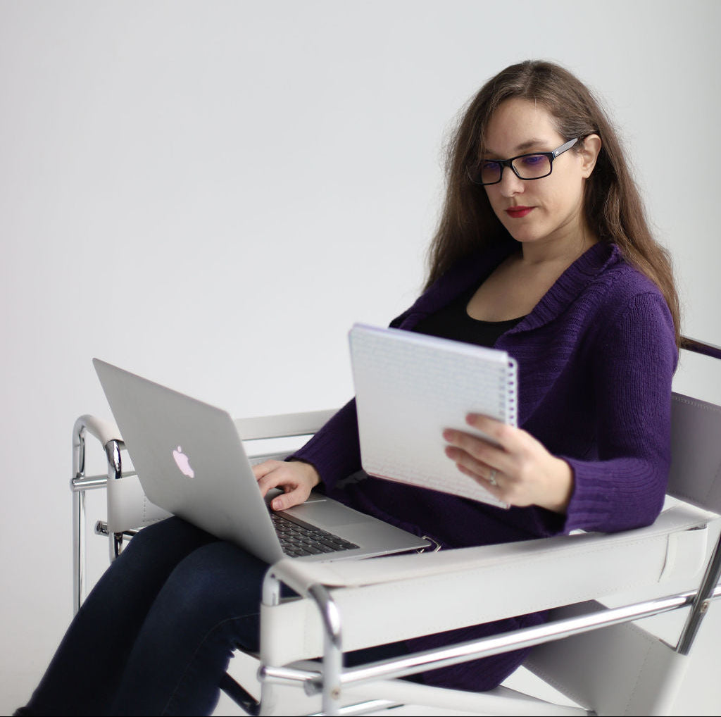 Woman sitting in a chair with a laptop and notebook on a white background